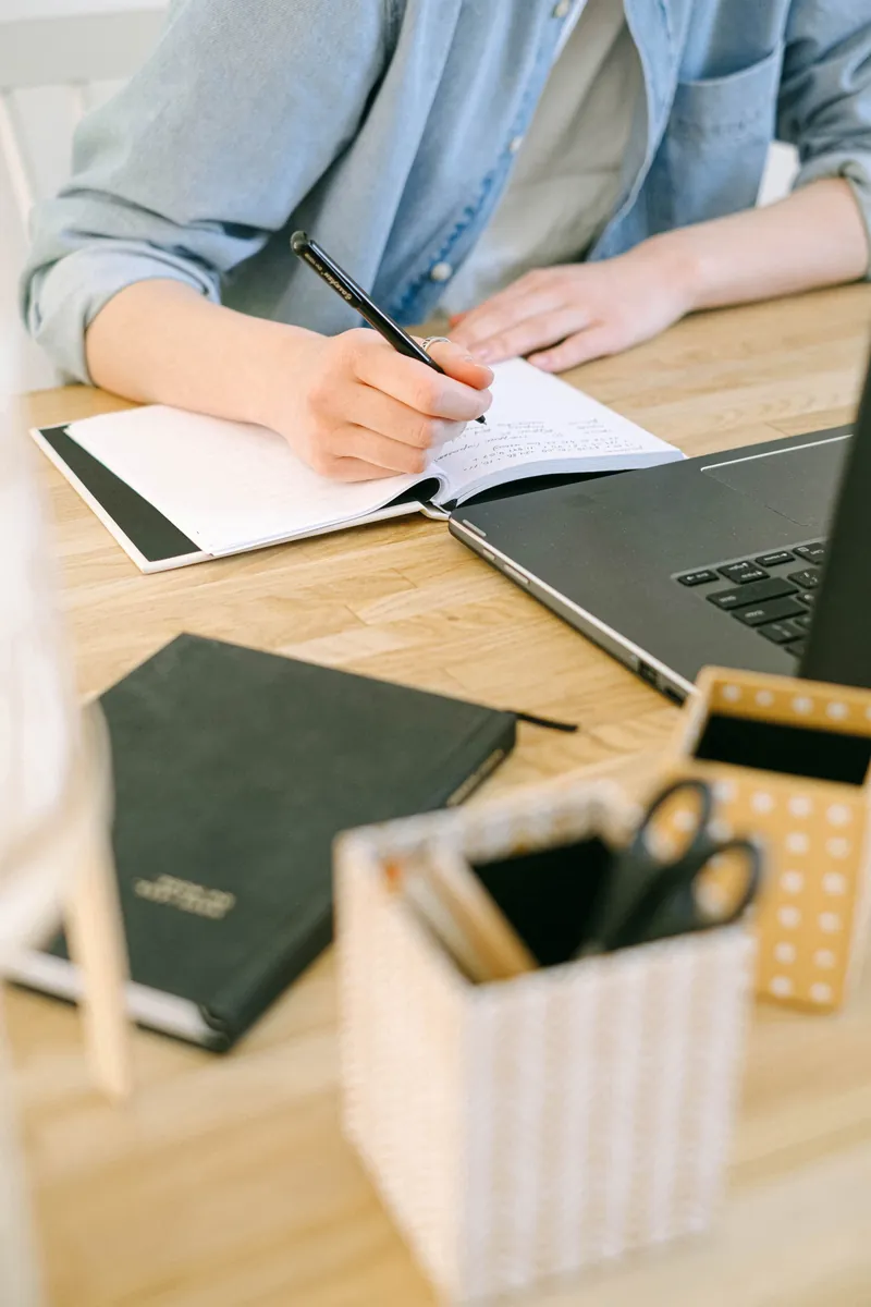 Learner taking notes beside a laptop